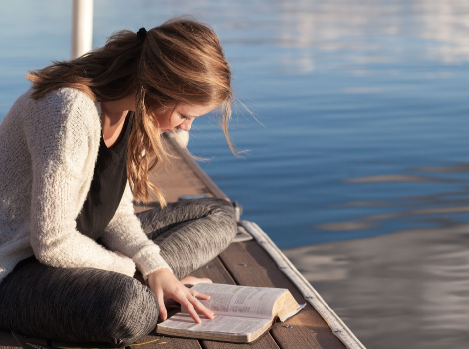 Dívka sedící u vody čte písma